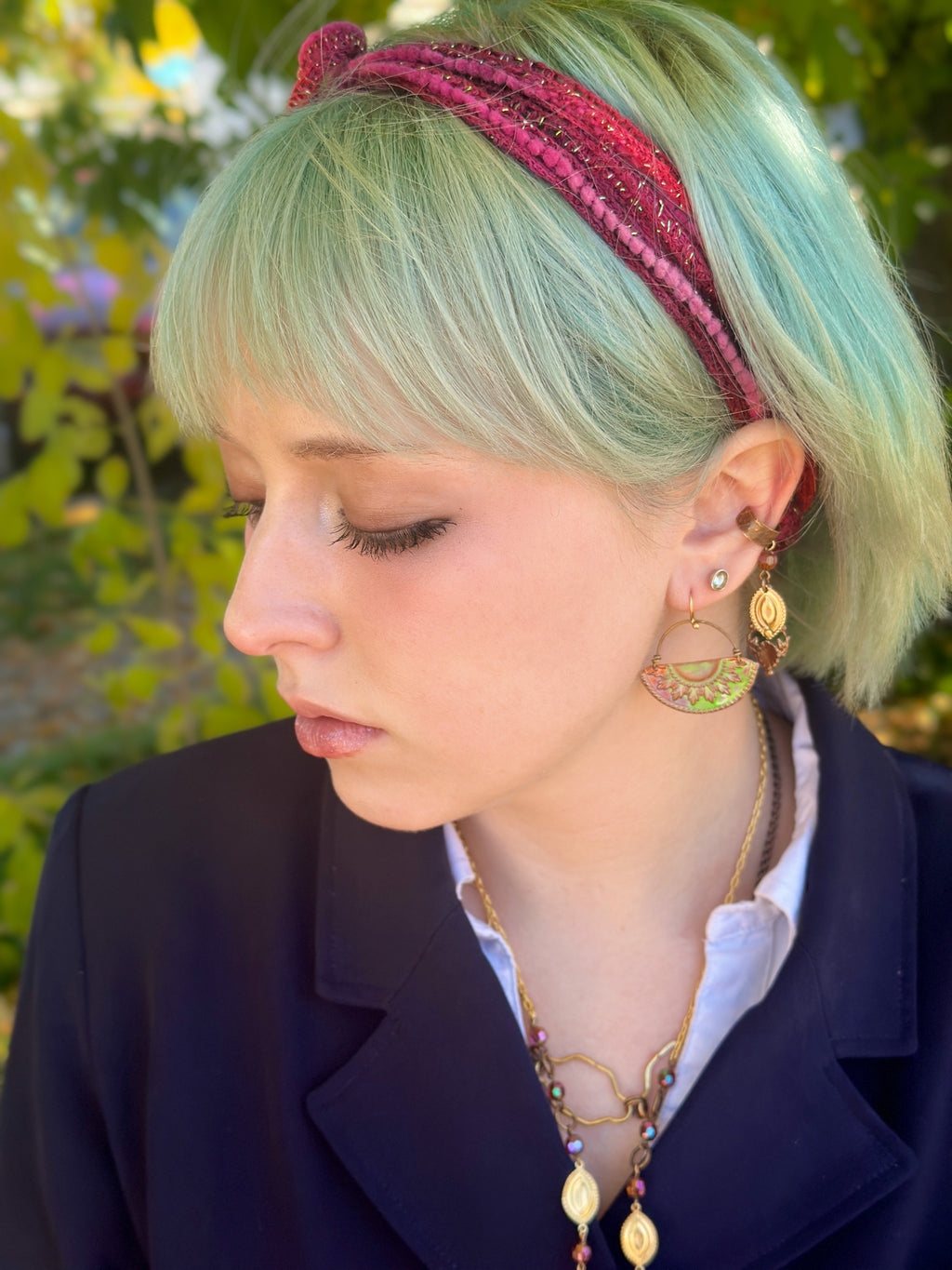 Woman with green hair wearing a headband and earrings.