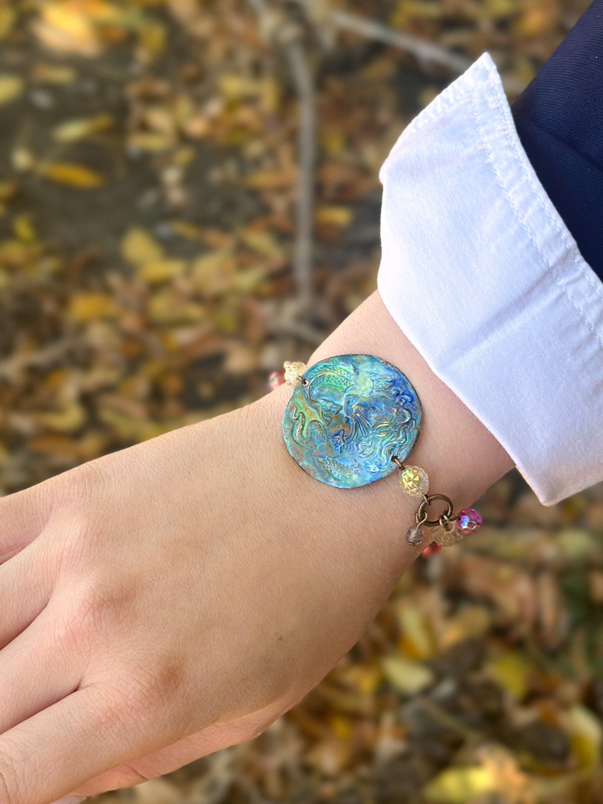 Bracelet on wrist with blue circular pendant.
