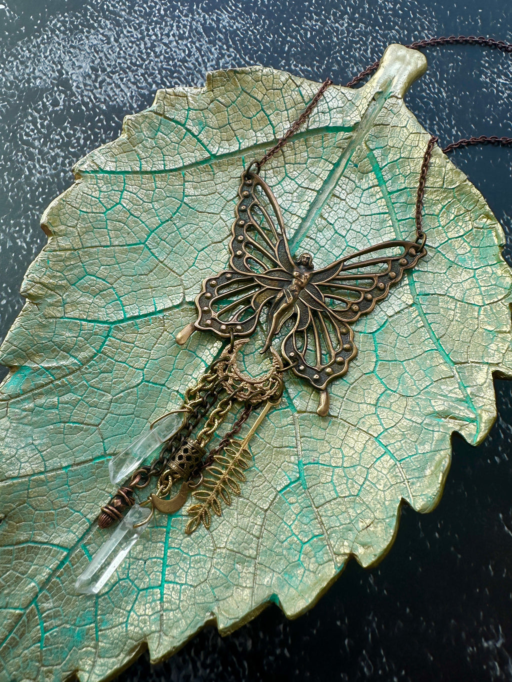 Butterfly pendant necklace on a leaf-shaped dish.