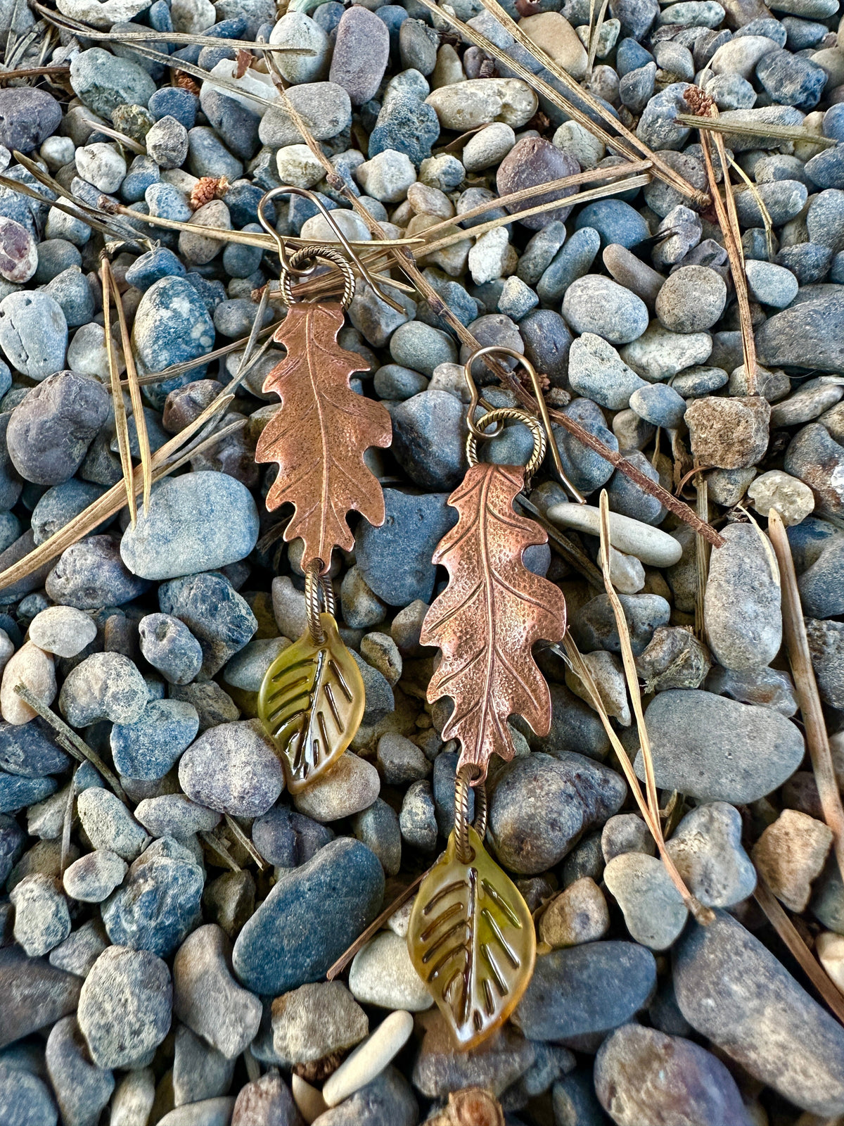 Leaf-shaped copper earrings on a bed of pebbles.