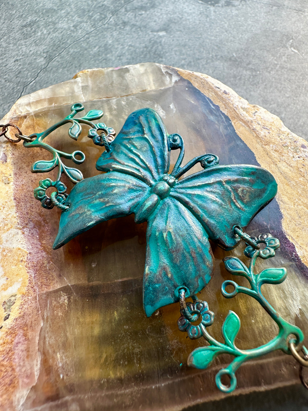 Teal butterfly necklace with floral accents.