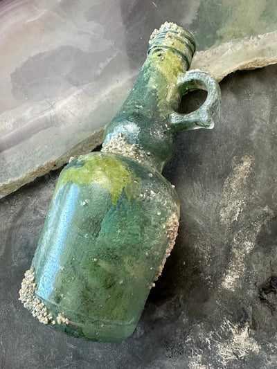 Green glass bottle with handle, covered in barnacles.